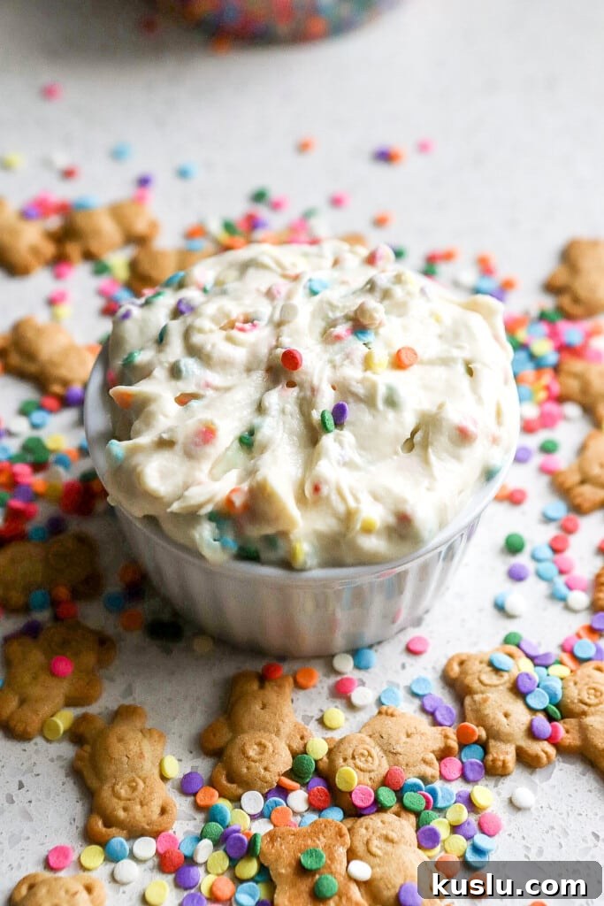 High-Protein Dunkaroo Dip: 5-Minute Party Snack 6 Side angle of a lighter dunkarro dip recipe in a small white ramekin with rainbow sprinkles and teddy grahams.