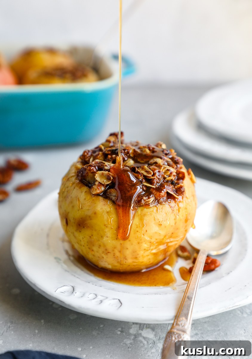 A baked apple stuffed with oat crumble and drizzled with honey sauce sitting on a white plate with a spoon