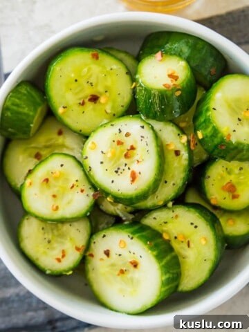 A bowl of Din Tai Fung cucumber salad topped with chili flakes and with a spoon beside it.