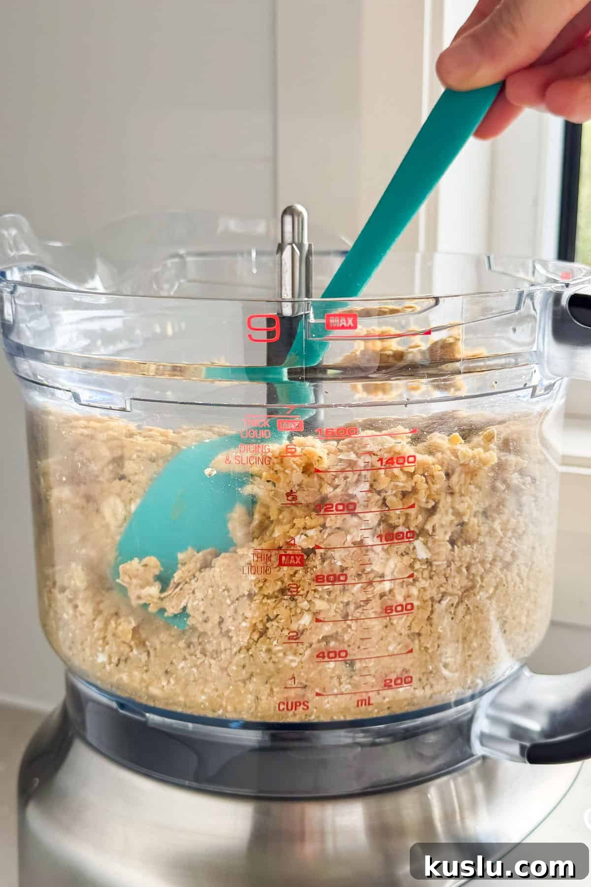 Cracker dough being pushed down in food processor with spatula.