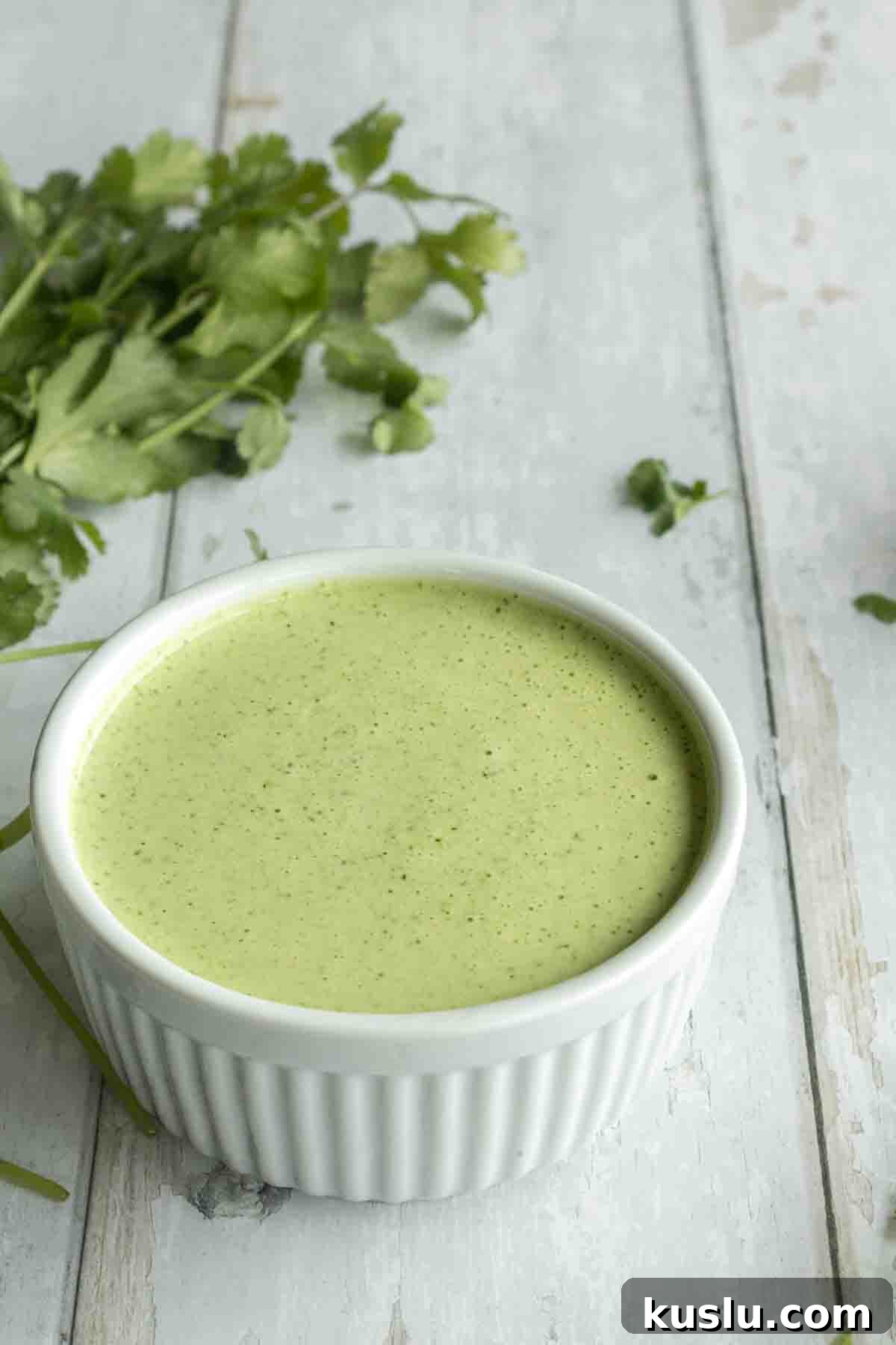 Cilantro Lime Crema: Creamy Sauce Recipe for Tacos & Bowls 2 A bowl of cilantro lime crema next to cilantro.