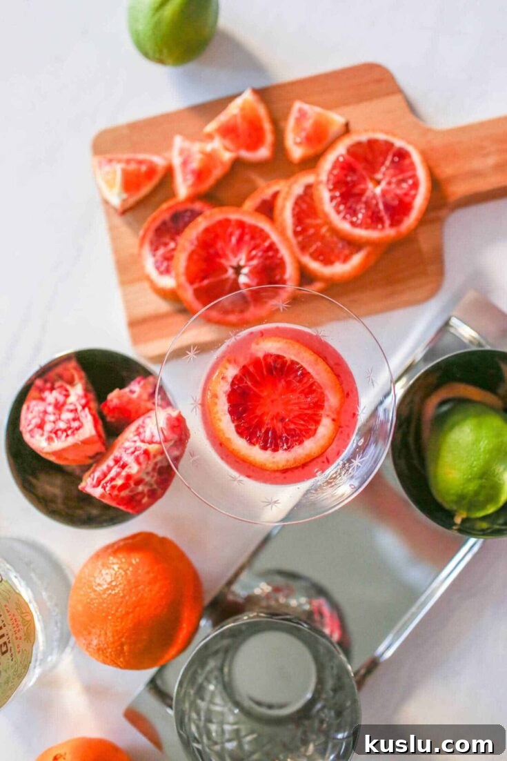 A blood orange martini on a white table next to freshly sliced blood oranges.