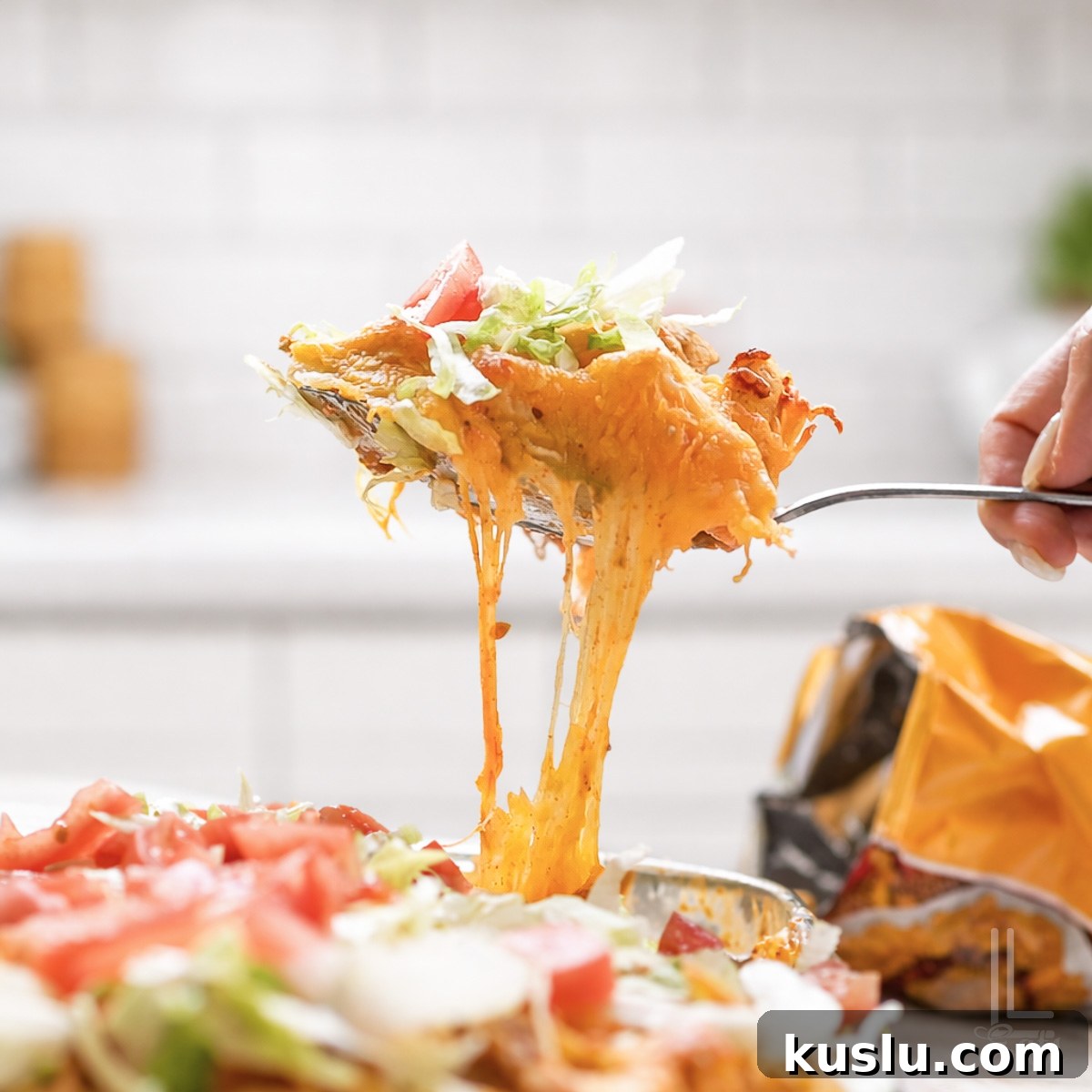 Walking Taco Casserole: Cheesy Taco Bake with Crunchy Nacho Topping 2 holding a spoonful of cheesy walking taco casserole topped with lettuce and tomato.