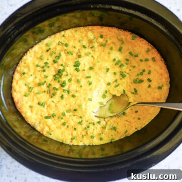 crock pot corn casserole in a slow cooker, with a spoon.