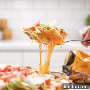 Walking Taco Casserole: Cheesy Taco Bake with Crunchy Nacho Topping 17 holding a spoonful of cheesy walking taco casserole topped with lettuce and tomato.