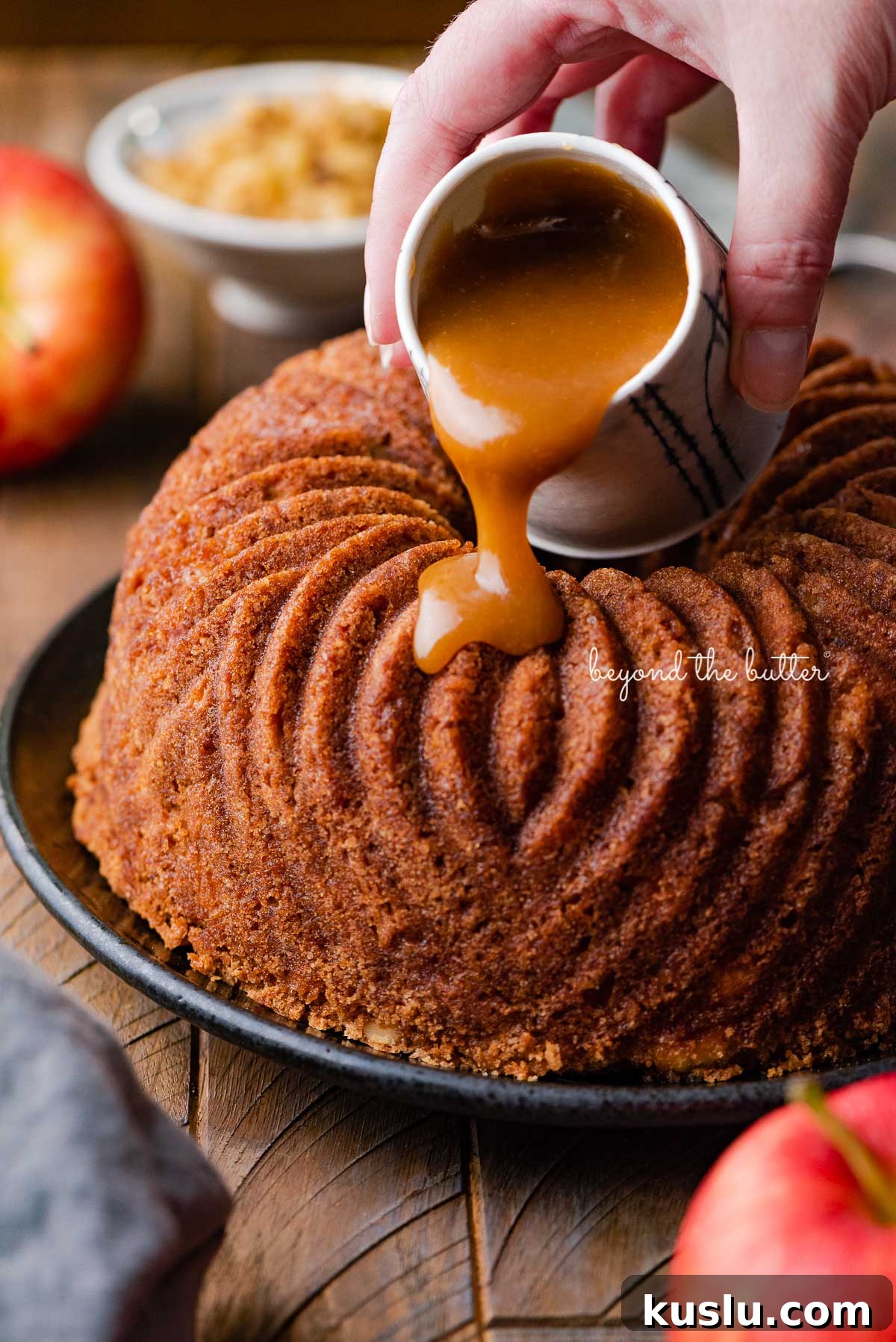 Pouring brown sugar glaze over top of warm apple bundt cake | © Beyond the Butter®