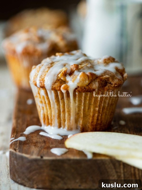 Warm apple cinnamon streusel muffins on a wood cutting board with slices of apples and vanilla glaze.