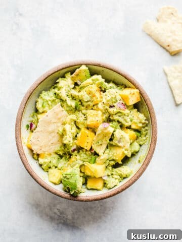A bowl of guacamole with mango chunks.