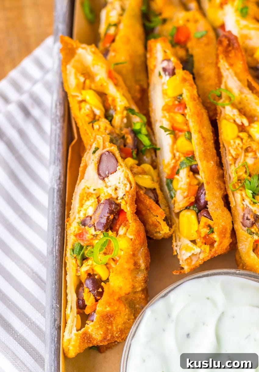 Southwestern Egg Rolls Copycat Recipe — Chili’s-Style Appetizer 3 cut southwestern egg rolls on a metal tray with a glass bowl of cilantro sour cream on the side