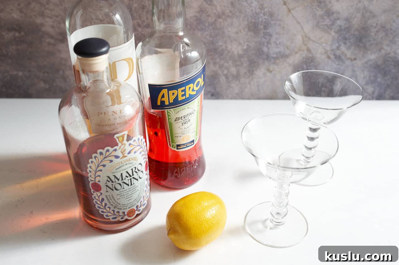 Bottles of amaro, aperol, and bourbon, next to a lemon and two martini glasses.