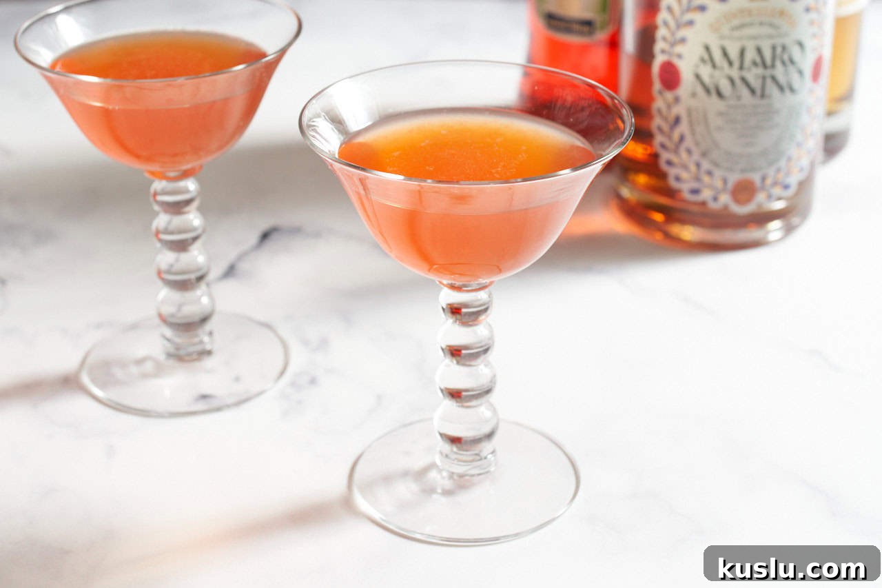 Two paper plane cocktails with bottles of liquor in the background.