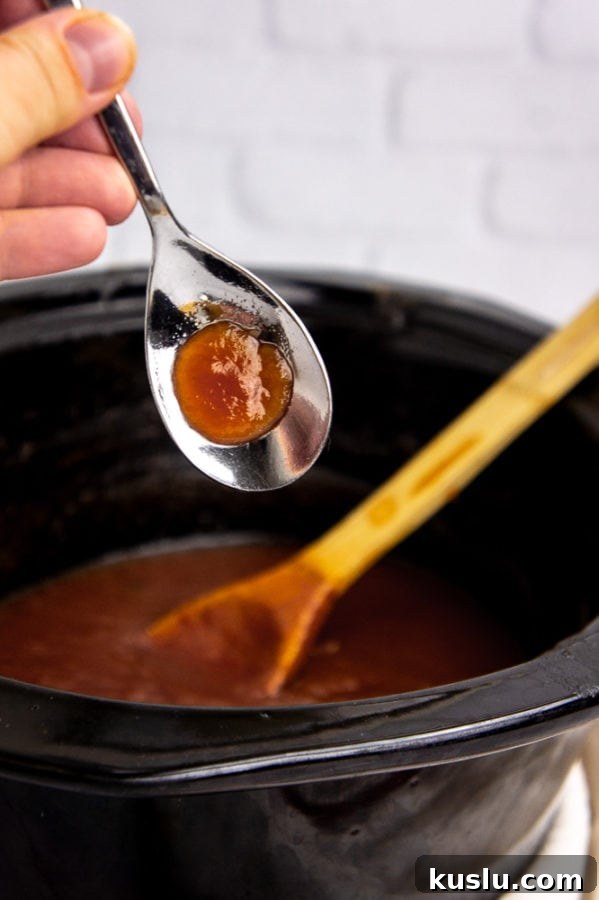 Slow Cooker Apple Butter Recipe for Canning and Preserving 6 a metal spoon with a dollop of apple butter on it over a crock pot with more apple butter in it