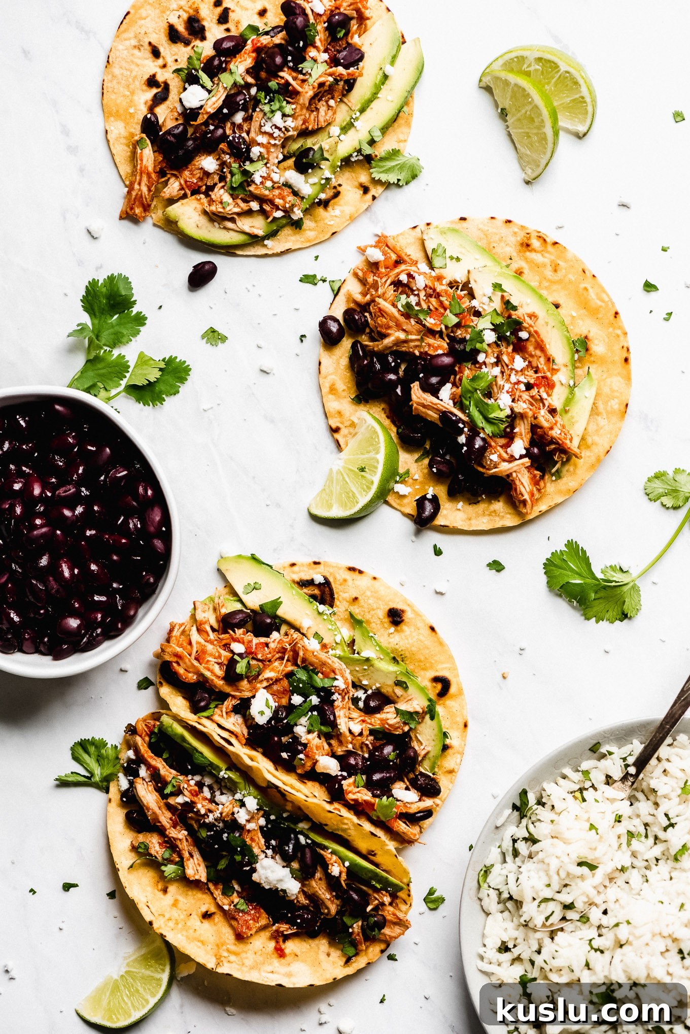 Salsa Chicken Tacos served with sides Instant Pot Salsa Chicken Tacos on a marble surface with bowl of cilantro lime rice and a bowl of black beans.