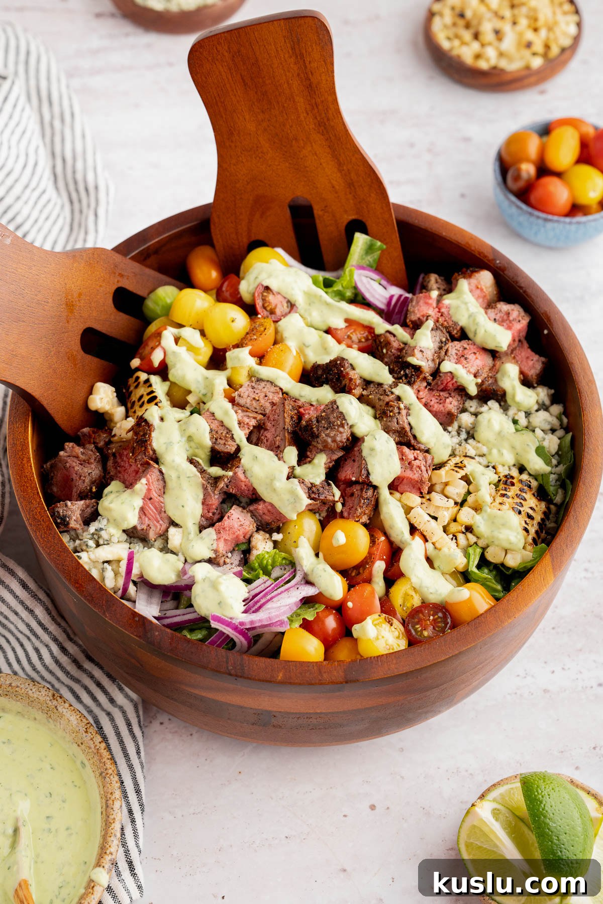 Grilled Steak Salad with Avocado-Lime Cilantro Crema 12 The steak salad with the avocado-lime cilantro crema drizzled on top in a bowl on a countertop. Two serving forks sit inside the bowl.