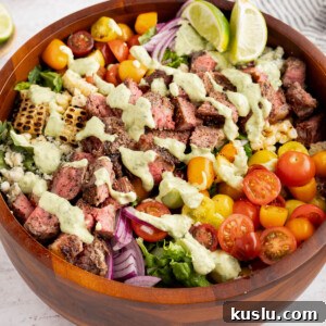 Grilled Steak Salad with Avocado-Lime Cilantro Crema 13 The steak salad with cilantro-lime avocado crema drizzled on top in a wooden bowl on a white countertop.