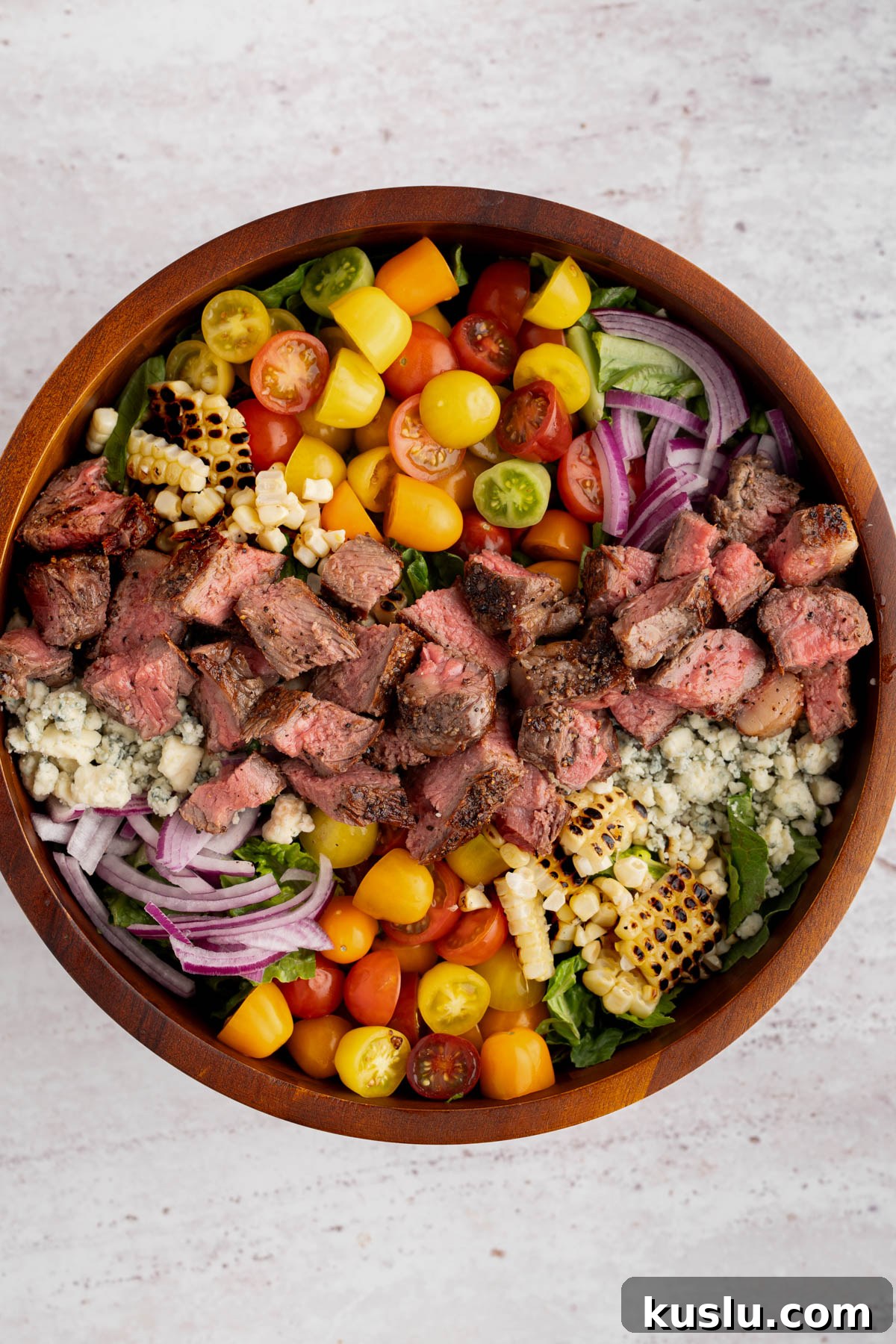 Grilled Steak Salad with Avocado-Lime Cilantro Crema 10 The fully assembled steak salad without the dressing in a bowl on a white countertop.