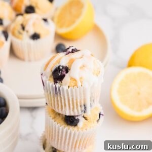 Golden lemon blueberry muffins baked and then stacked on the table with lemons stacked behind the muffins.