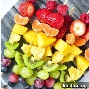 Pieces of fruit skewered in a rainbow color pattern on a small light gray cutting board.