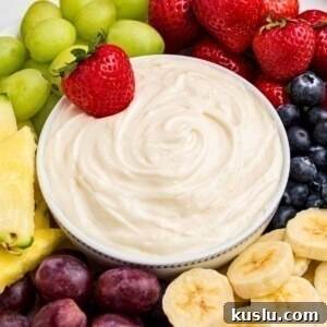 White bowl with fruit dip, surrounded by grapes, bananas, blueberries, and other fruits.