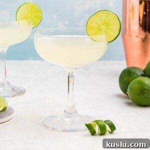 Coupe glass filled with drink, garnished with lime wheel, on a marble table with a blue backdrop.