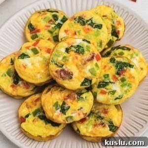 Bright yellow egg bites with red and green chopped bell peppers baked inside, on a round cream plate.