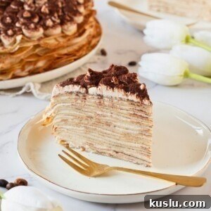 Golden light and fluffy slice of cake made from layers of thin crepes, served on a white plate.