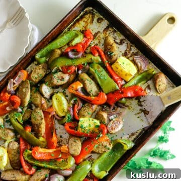Sausage and peppers on a baking sheet, with two white plates and utensils on the side.