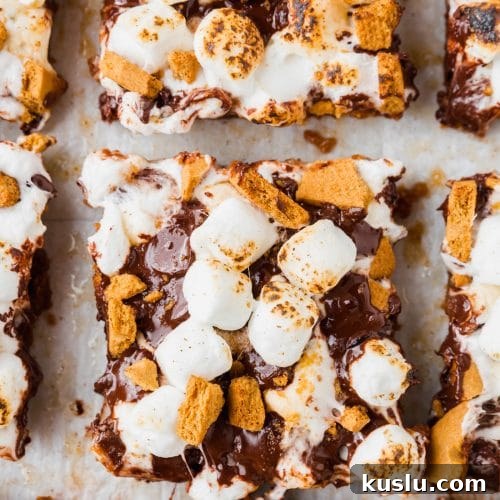 Gluten-Free S’mores Bars Recipe — Chewy Graham & Chocolate Squares 8 An overhead view of sliced gluten-free smores bars topped with graham crackers and marshmallows on a piece of parchment paper.