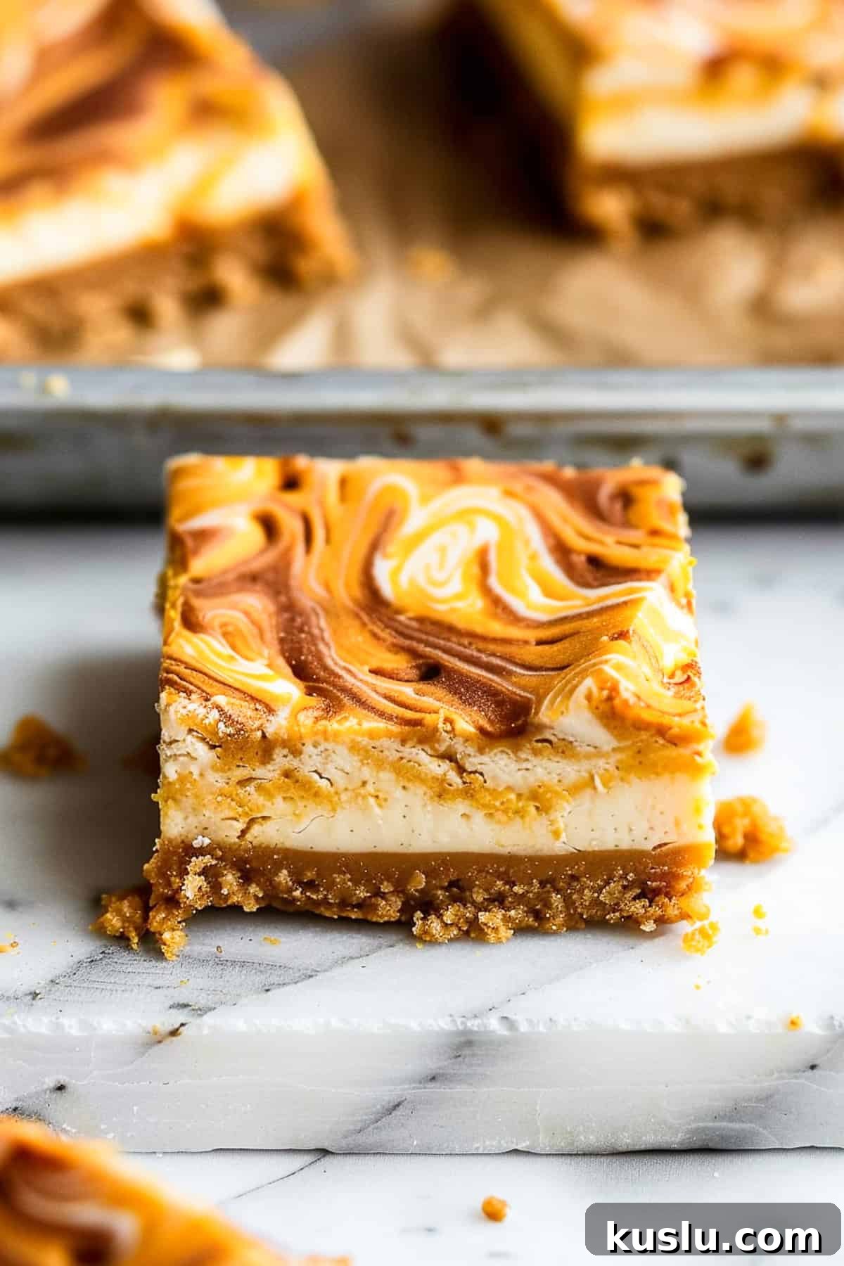 Pumpkin swirl cheesecake bars on a marble cutting board with nutmeg and cinnamon.