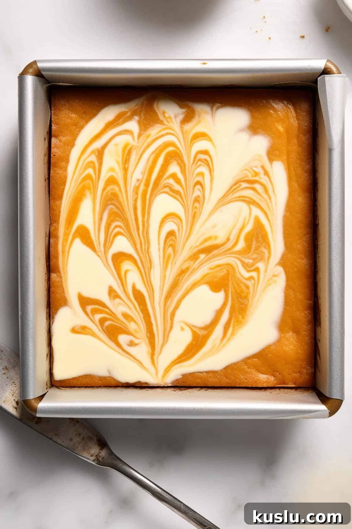 Pumpkin swirl cheesecake bars in a square tin before being cut.