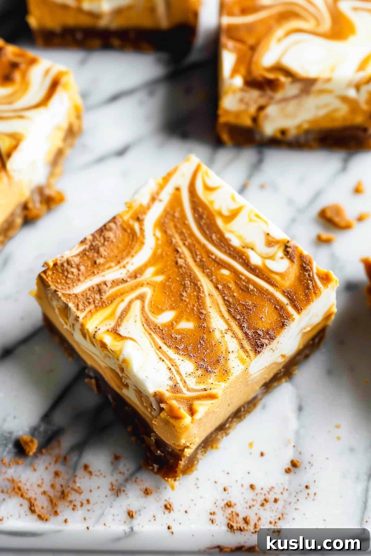 Pumpkin swirl cheesecake bars on a marble cutting board with nutmeg and cinnamon.