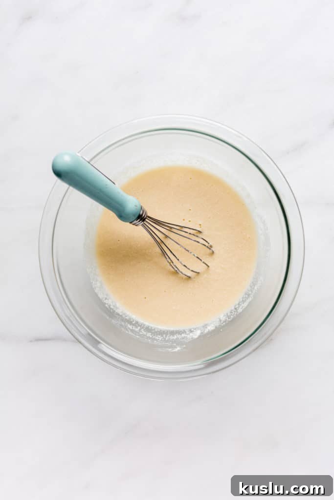a clear mixing bowl with coconut flour pancake batter and a whisk in it