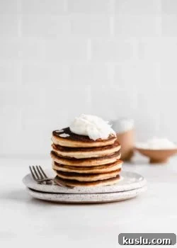 a stack of coconut flour pancakes on a white speckled plate with a fork on the side