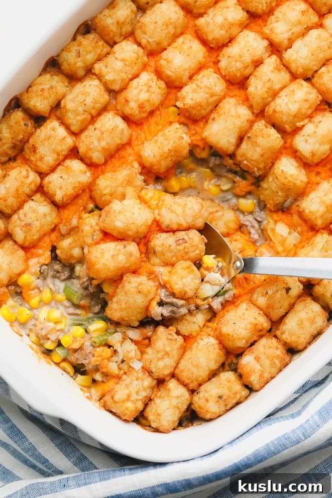 metal spoon scooping some baked tater tot casserole out of a white casserole dish.