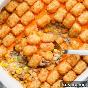 metal spoon scooping some baked tater tot casserole out of a white casserole dish.