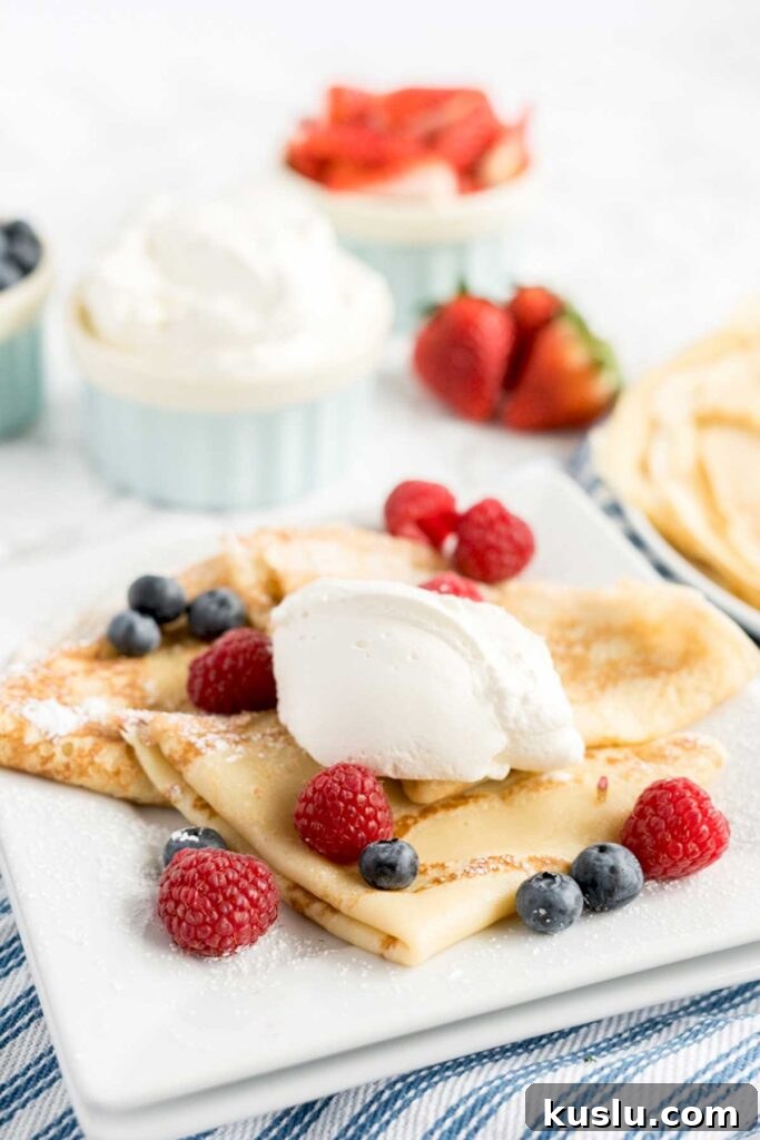 A serving of sweet French pancakes topped with whipped cream and berries.
