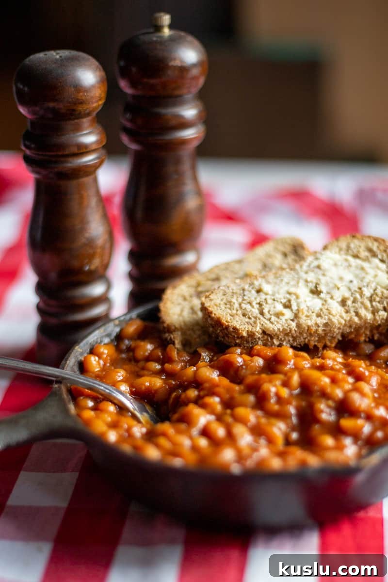 Scratch-Made Baked Beans Recipe for Rich, Slow-Cooked Flavor 2 Baked beans in cast iron skillet with salt and pepper shakes on the side.