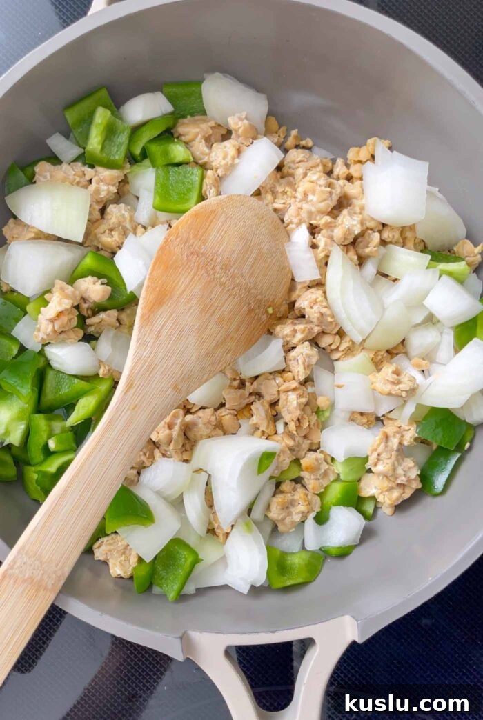 Chopped onion, bell pepper and crumbled tempeh cooking in a pan.