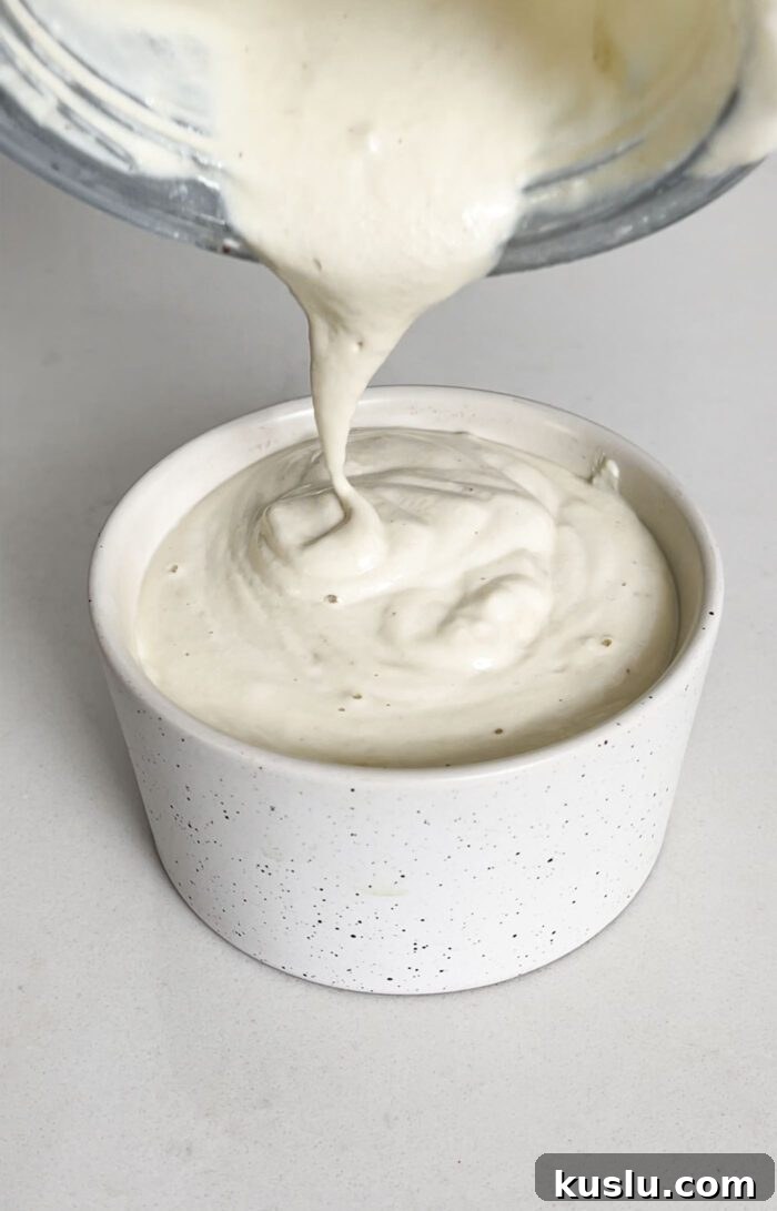 Pouring creamy sauce from a blender container into a small dish.
