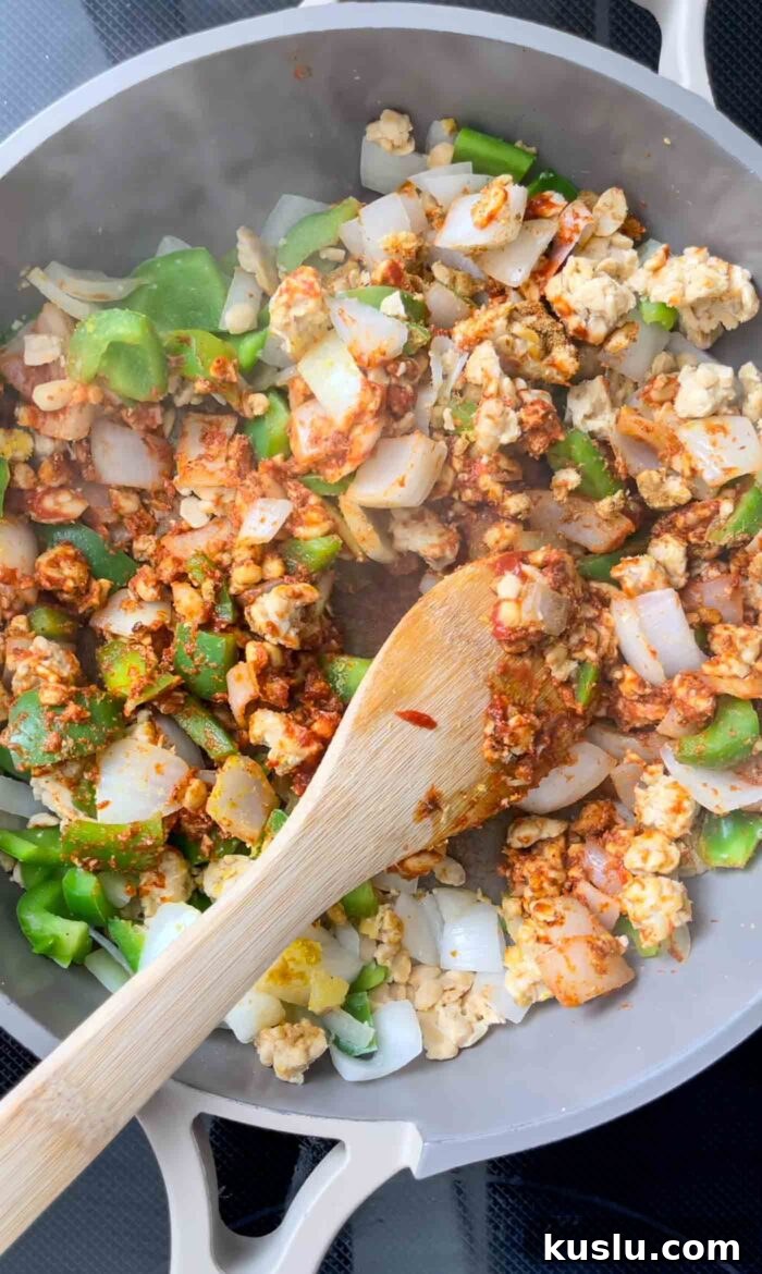 Onion, green bell pepper and tempeh cooking in tomato paste and spices in a skillet.