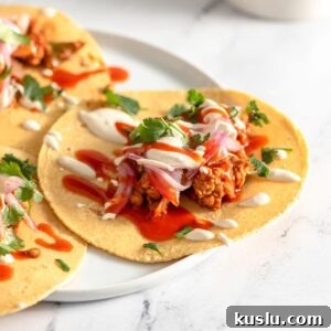 Three vegan tempeh tacos topped with pickled onion, cashew crema and hot sauce on a plate.