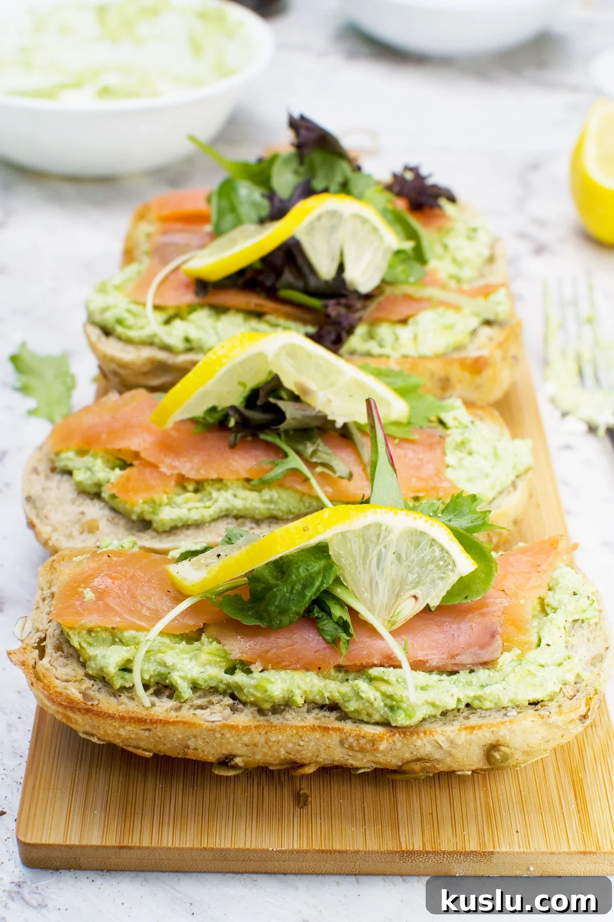 4 smoked salmon bruschettas with smashed avocado and feta on a wooden chopping board
