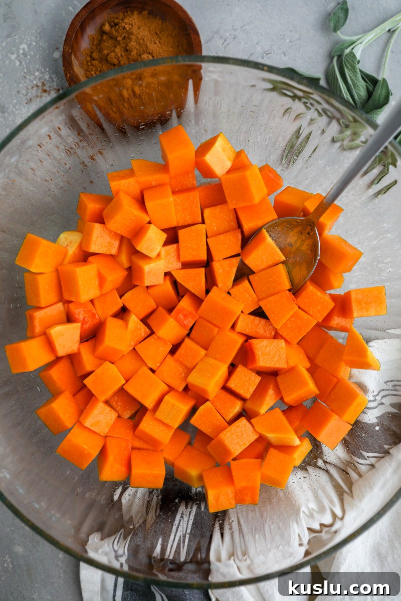Maple Brown Butter Roasted Butternut Squash Recipe 5 A large clear mixing bowl filled with diced butternut squash tossed in olive oil and salt