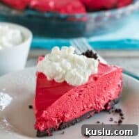 Slice of no bake red velvet cheesecake with the rest of the cheesecake in the background.