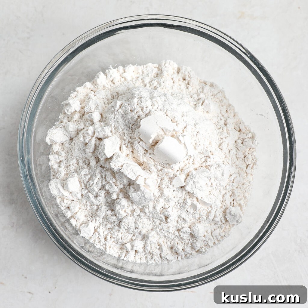 A glass bowl filled with flour and several small chunks of white solid shortening or butter, set on a light-colored surface—perfect for starting a batch of Maple Blondies.