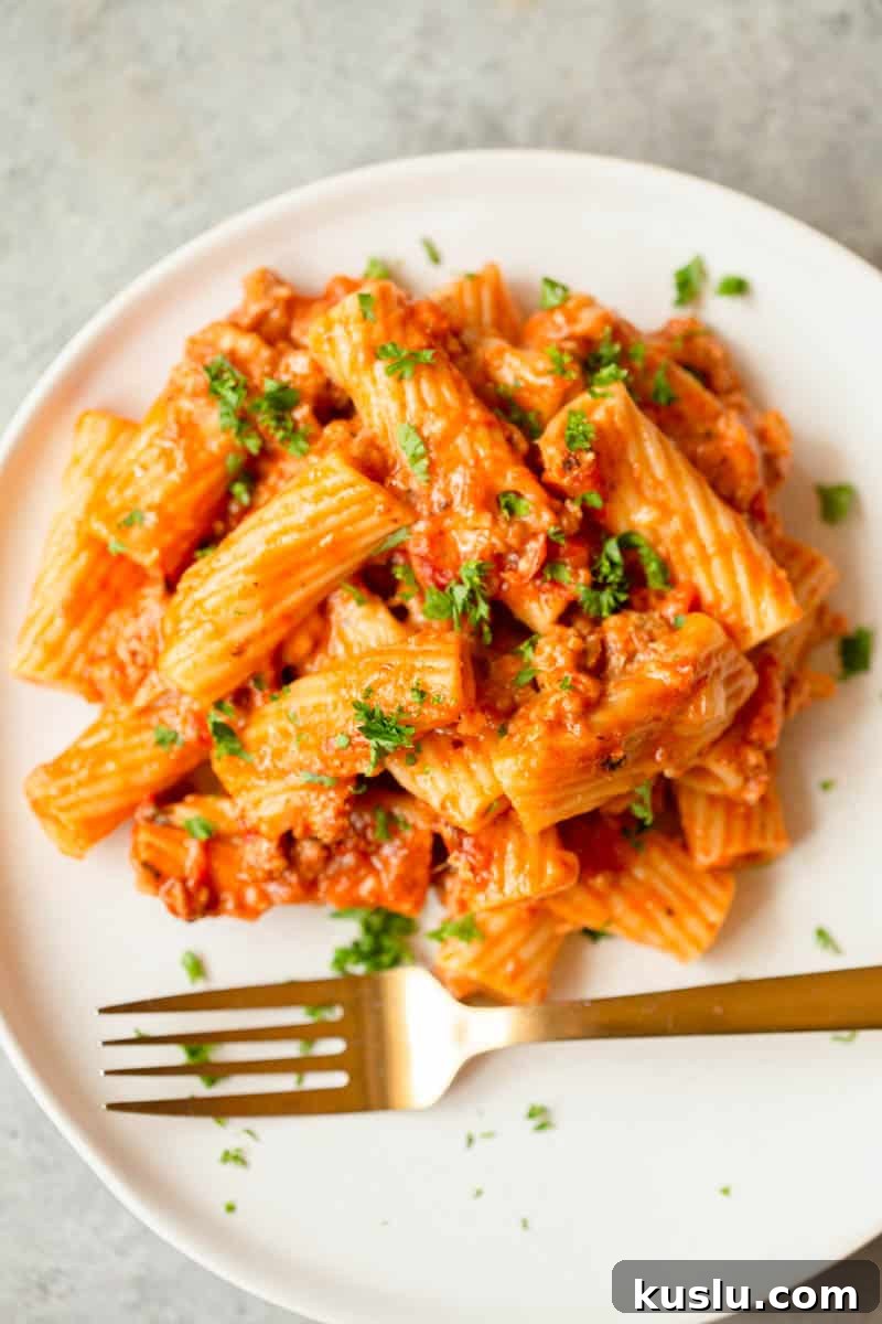 Instant Pot Sausage Rigatoni on a white plate on a gray background with a gold fork. 