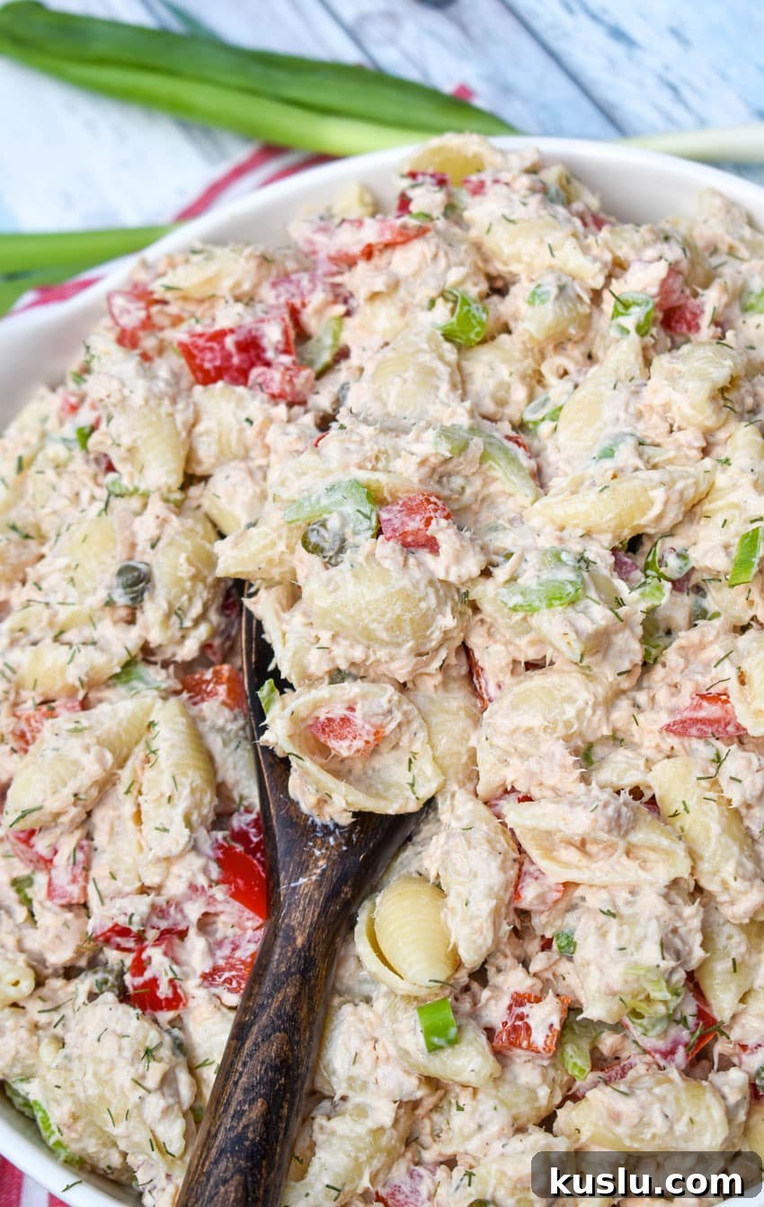 A wooden spoon scooping canned salmon pasta salad out of a white serving dish