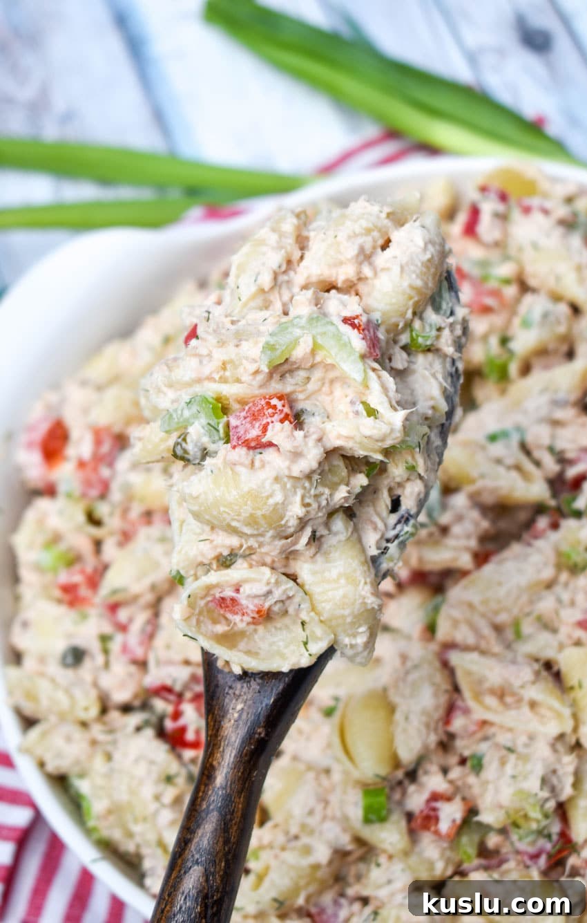 a wooden spoon holding up a scoop of canned salmon pasta salad
