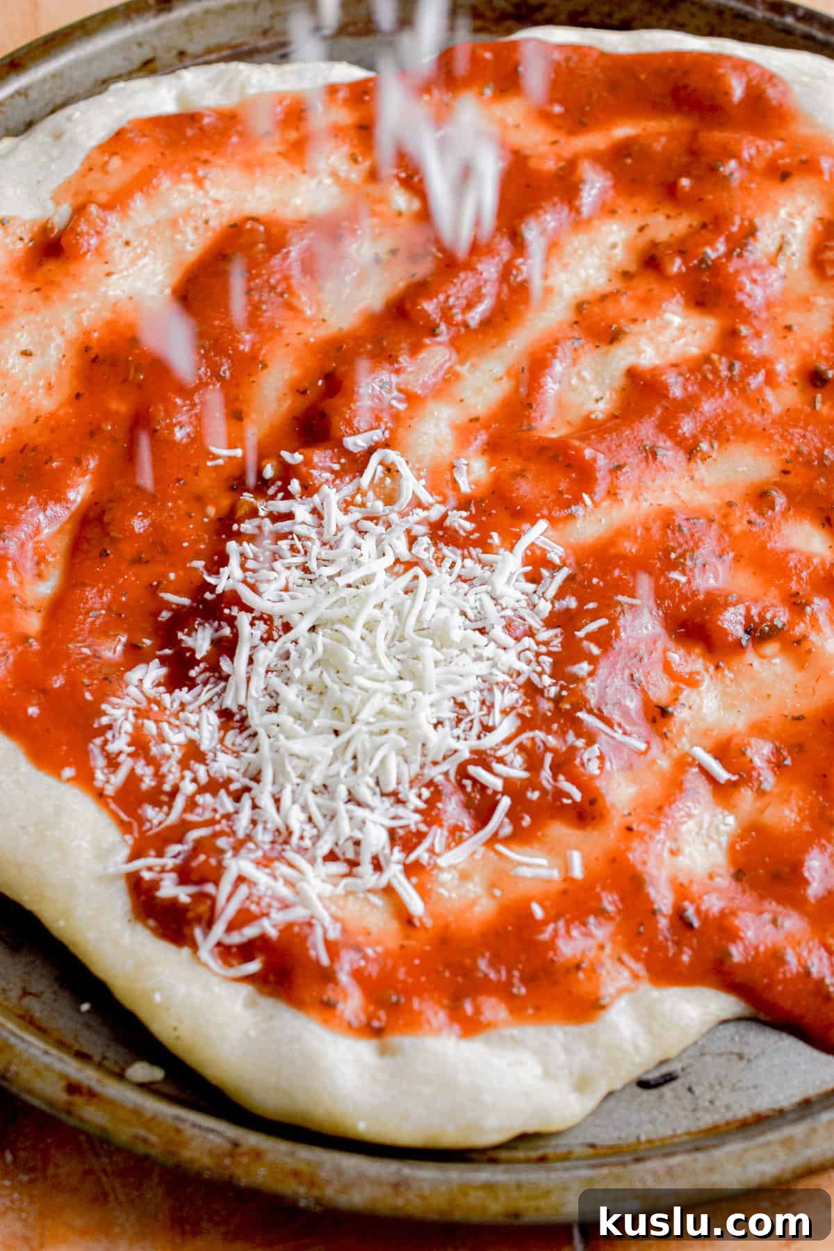 Sourdough Cast-Iron Pizza Without Yeast: Crispy Homemade Pie 11 Cheese is being sprinkled on the sauce.
