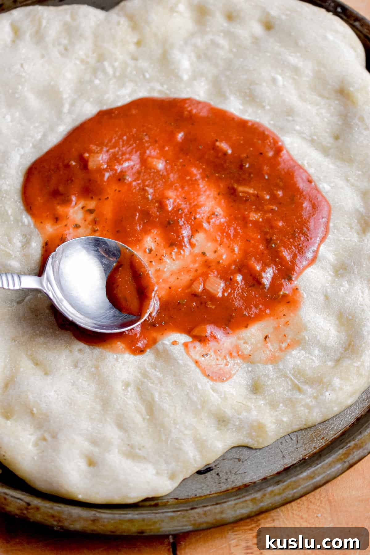 Sourdough Cast-Iron Pizza Without Yeast: Crispy Homemade Pie 10 A spoon is spreading the sauce on the sourdough pizza dough.